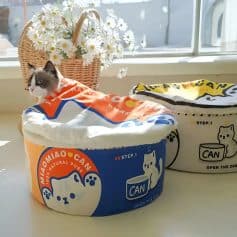 Cute cat resting on colorful pet food containers with a flower basket in the background.