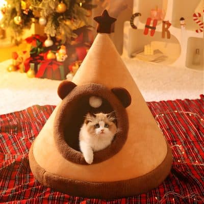 Cozy cat bed shaped like a tepee with a kitten inside, decorated for Christmas with festive background, holiday ornaments, and a decorated tree, perfect for pet comfort and holiday home decor.