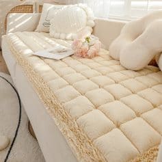 Soft beige plush mattress topper with ruffled edges, decorative cushions, and fresh flowers on a white sofa, creating a cozy, stylish bedroom decor scene. Suitable for enhancing comfort and aesthetics.