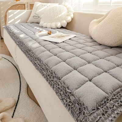 Plush gray quilted mattress topper with ruffled trim on a white bed, decorated with cozy pillows, pastel tones, and natural sunlight for a relaxing bedroom ambiance.