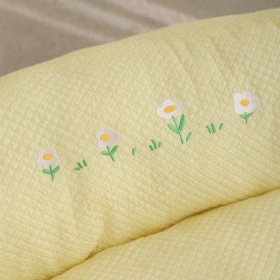 Colorful floral embroidery on pastel yellow quilted bedding, soft texture, decorative bed linen for bedroom decor.