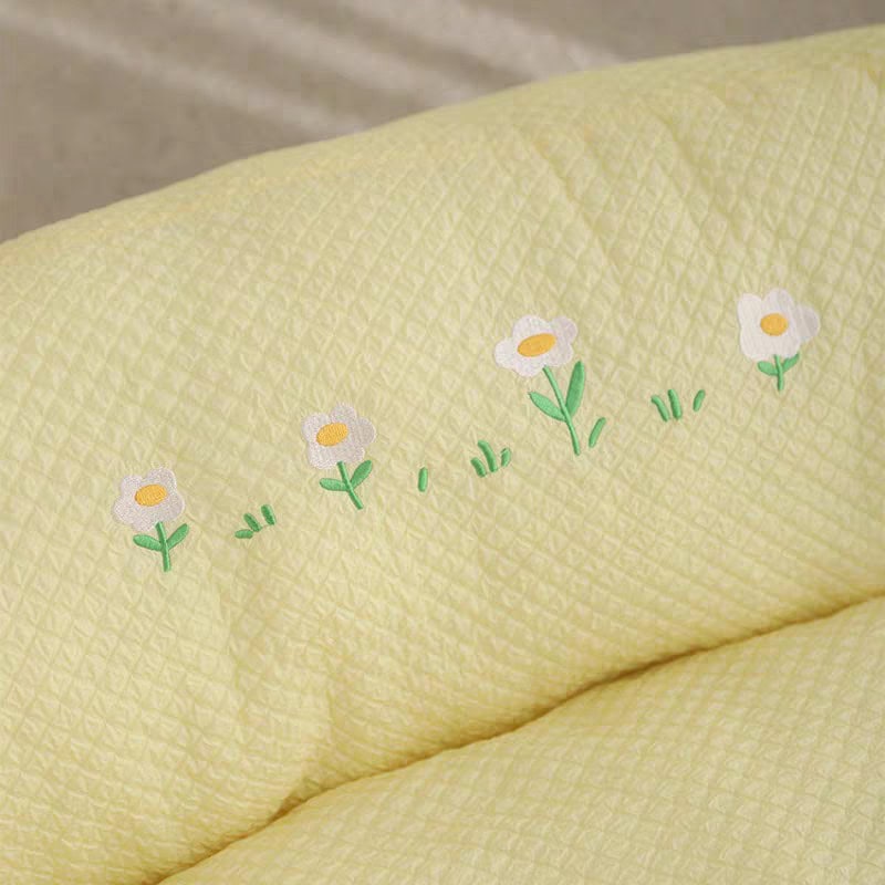 Colorful floral embroidery on pastel yellow quilted bedding, soft texture, decorative bed linen for bedroom decor.