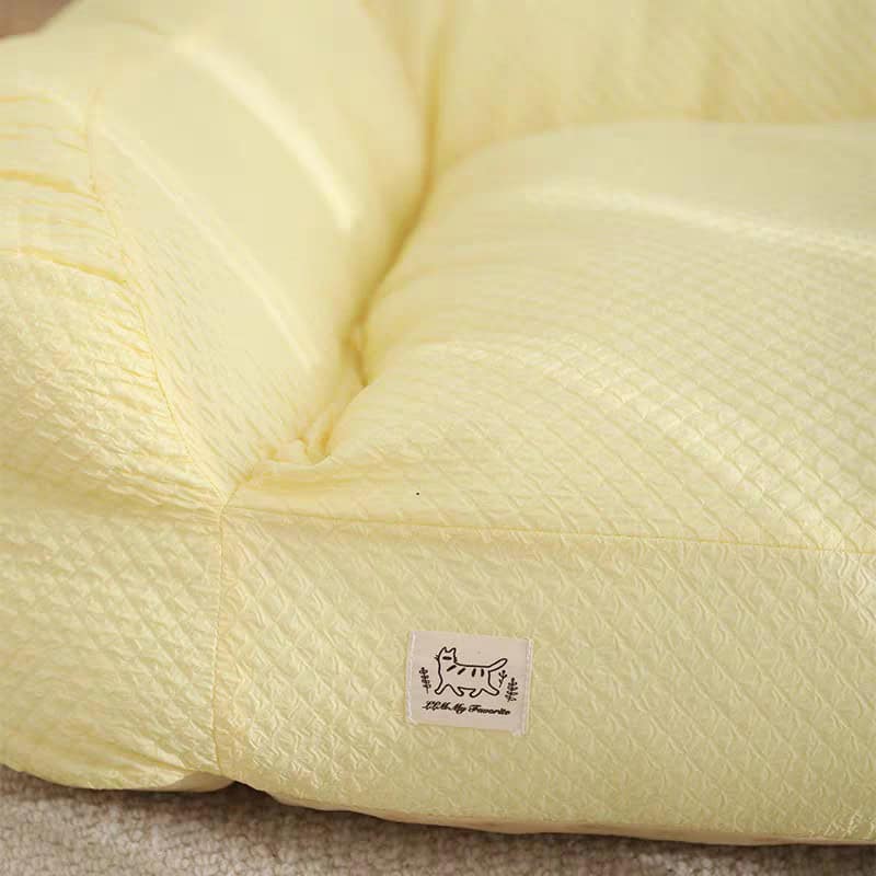 Soft yellow plush cushion with a stitched logo of a playful cat, featuring subtle diamond pattern textures, designed for comfort and aesthetic appeal in home or store decor.