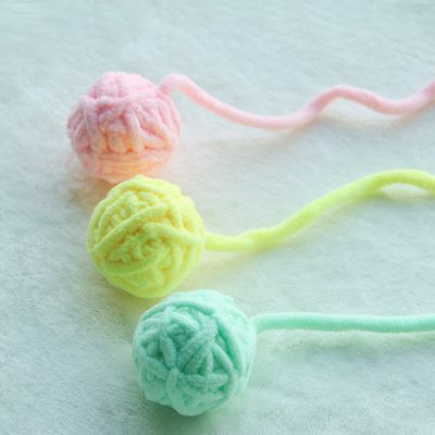 Colorful yarn balls in pastel pink, yellow, and mint green, suitable for knitting or craft projects, arranged on a soft, textured background.