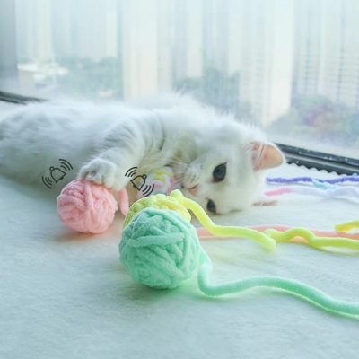 Colorful yarn balls and a playful white cat at Monalisa Store, showcasing pet accessories and toys for cats, ideal for pet lovers and owners seeking quality supplies.