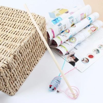 Woven basket with wooden stick, colorful rolled papers and cat toy on white surface, promoting Monalisa Store's optical and eyewear accessories.