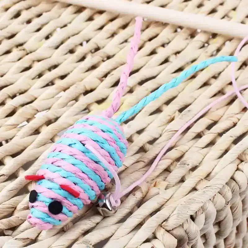 Pink and blue yarn mouse keychain on woven straw background, cute animal accessory, handmade craft, perfect for children or animal lovers.