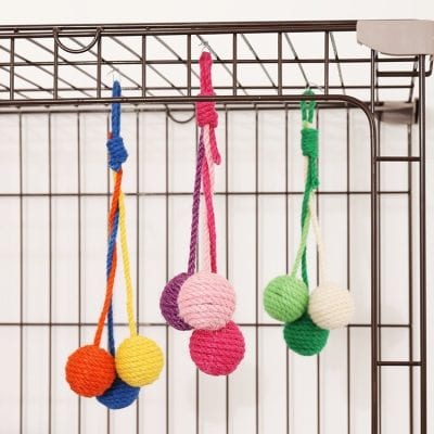 Colorful knitted balls on strings hanging inside a metal pet cage, likely for a cat or small pet entertainment and enrichment.