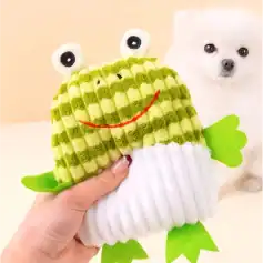 Bright green and white plush frog toy with googly eyes, smiling face, and felt limbs, held in a person's hand with adorable white puppy in the background.