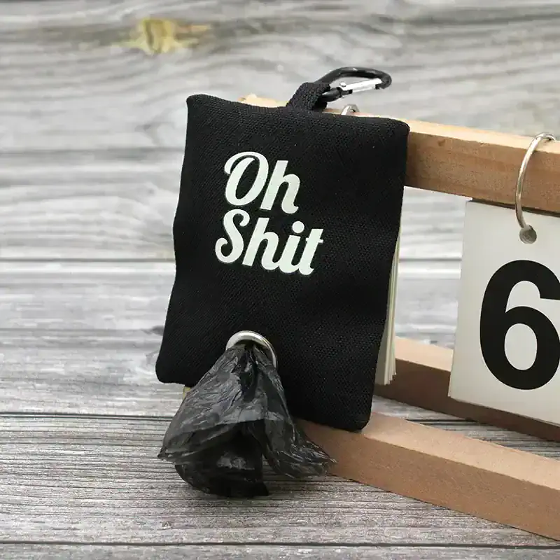 Oh Shit pouch with a black color and white text, attached to a keychain, placed on a rustic wooden surface, humorously designed for eye-catching accessories or gift items.