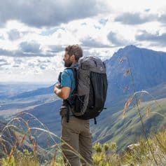 Backpacking man hiking in mountain landscape with large backpack, exploring nature, adventure, outdoor travel, trekking, and wilderness exploration.