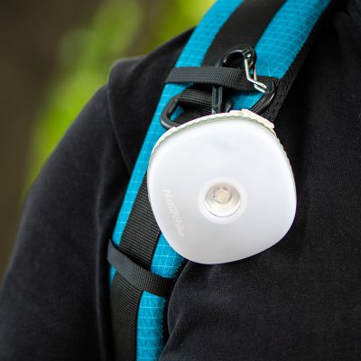 Compact LED flashlight for outdoor activities, attached to a hiking backpack with carabiner, portable lighting solution for hiking and camping.