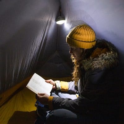 Family camping tent interior with woman reading book in warm outdoor clothing and bright yellow beanie, cozy camping setup, outdoor adventure, exploration, enjoying nature, winter camping, adventure gear, outdoor lifestyle, Monalisa Store.