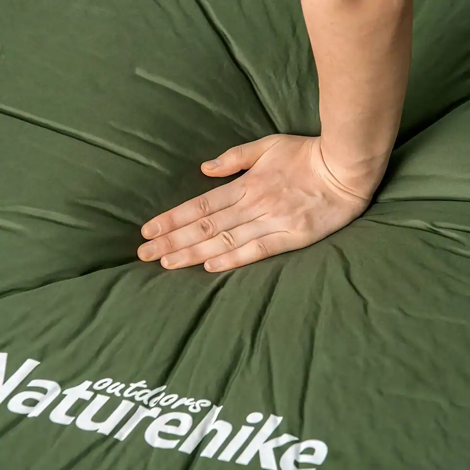 Hand pressing down on a green cushion with "Naturehike" branding, showcasing comfort and support, ideal for outdoor gear and camping accessories.
