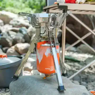 Compact portable camping stove with aluminum construction, perfect for outdoor cooking during camping and hiking adventures. Stainless steel windscreen surrounds the burner for added efficiency.