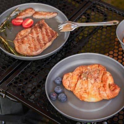 Grilled steak and salmon dishes served on gray plates with fresh blueberries and cherry tomatoes, placed on a black metal outdoor table for a delicious meal.