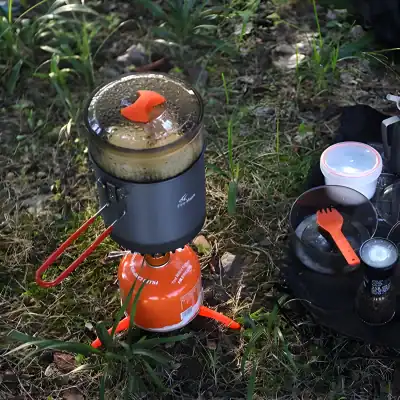 Boiling water and cooking outdoors with portable camping stove in a natural grassy environment.
