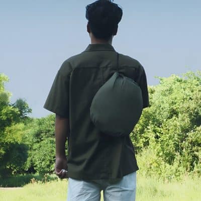 Back view of a young man in outdoor setting carrying a compact, black, foldable backpack on his shoulder, highlighting travel and daily use accessories from Monalisa Store.