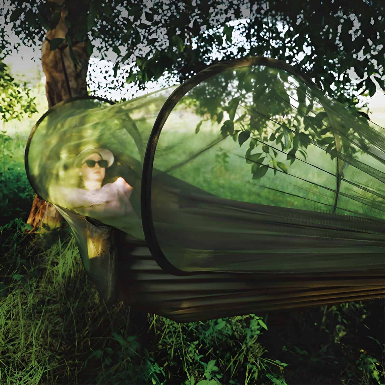 A woman relaxing in a portable outdoor sun tent with UV protection, wearing sunglasses and a sunhat, surrounded by lush greenery. Perfect for outdoor activities like camping, hiking, or backyard relaxation.