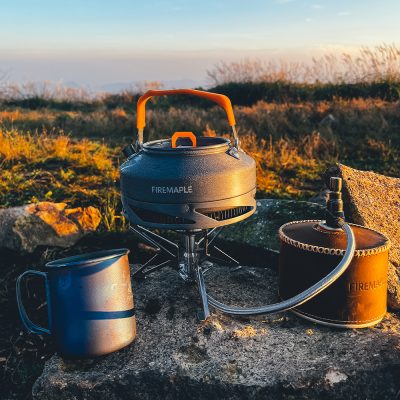 Compact portable camping stove with an orange handle and fuel canister, ideal for outdoor cooking and thermos for beverages. Perfect gear for camping, hiking, and outdoor adventures.