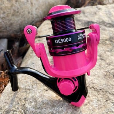 Vibrant pink fishing reel on a natural outdoor background, showcasing durable construction and smooth operation, ideal for freshwater and saltwater anglers seeking high-performance fishing gear.