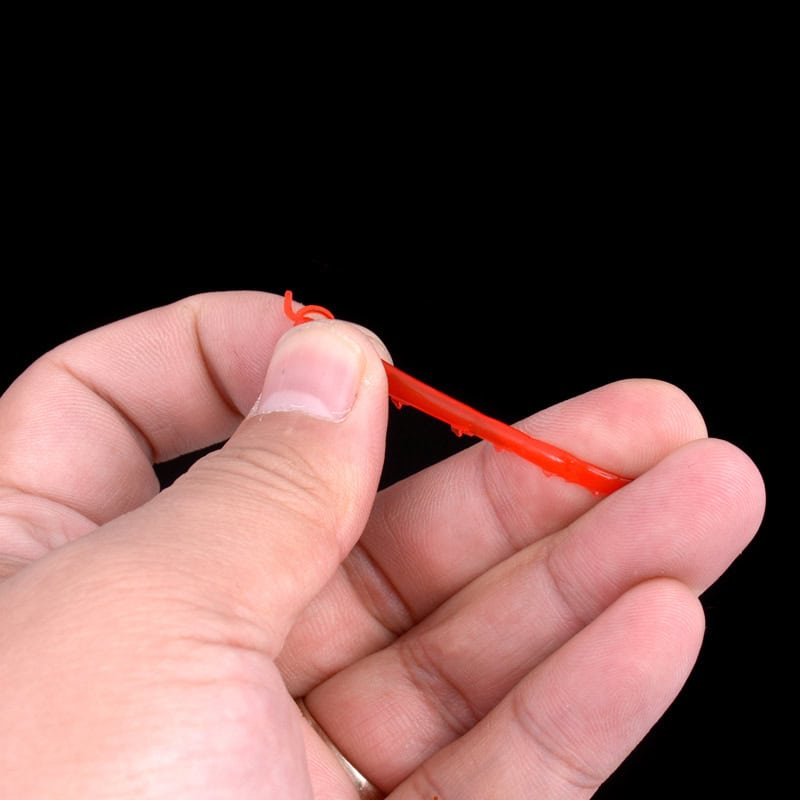 Flexible red dental floss pick being held in a hand with a black background, showcasing oral hygiene tools.