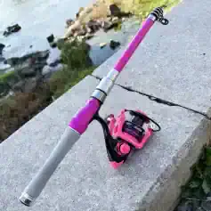 Pink fishing rod with reel on concrete by water, outdoor sight.