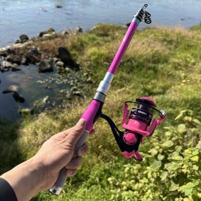 Pink fishing rod by the water with scenic nature background.