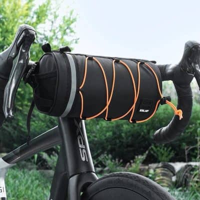 Waterproof bicycle handlebar bag for outdoor cycling accessories, black with orange bungee cords, designed for bike storage and organization, shown mounted on a bike handlebar outside in nature.
