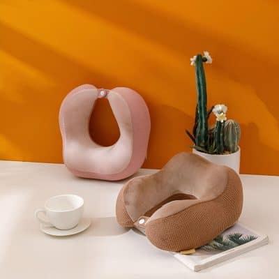 Memory foam travel neck pillows for comfort and support, stylish pink and beige colors, perfect for long trips and airport travel, displayed on a modern white surface with a cactus plant.