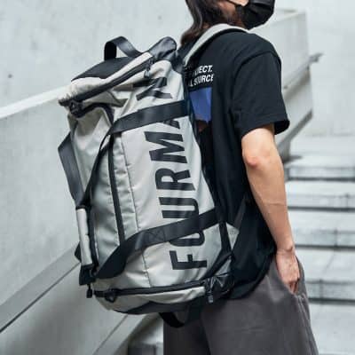 Blue and gray large travel backpack with black straps on a person wearing a black T-shirt and face mask, standing on outdoor stairs.