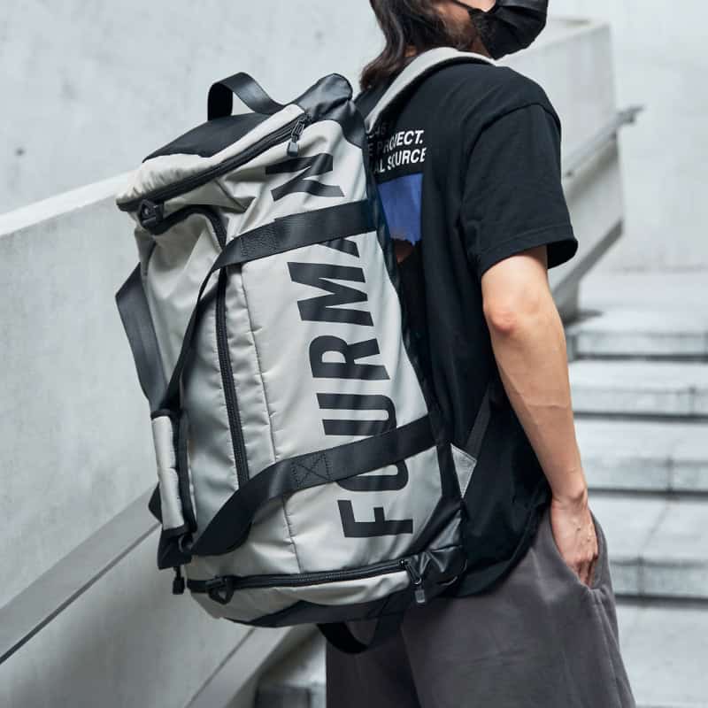 Blue and gray large travel backpack with black straps on a person wearing a black T-shirt and face mask, standing on outdoor stairs.