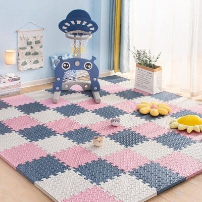 Colorful children's playroom with pink, blue, and white foam puzzle mats, featured with a mini basketball hoop, plush flower cushions, and playful toys for kids' entertainment and learning.