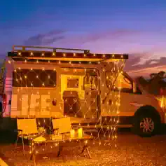 Fascinating illuminated mobile tiny home decorated with string lights and candles for cozy outdoor experience at dusk.