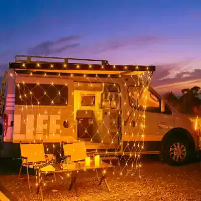 Fascinating illuminated mobile tiny home decorated with string lights and candles for cozy outdoor experience at dusk.
