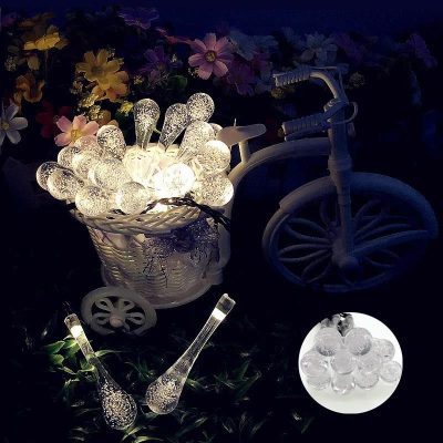 Glowing glass LED sphere lights in a decorative basket with miniature white tricycle and flowers for home decor or outdoor lighting.