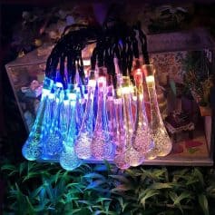 Colorful LED glass decanters illuminated with vibrant blue, pink, yellow, and white lights, displayed on a shelf surrounded by greenery and decorative items at Monalisa Store.