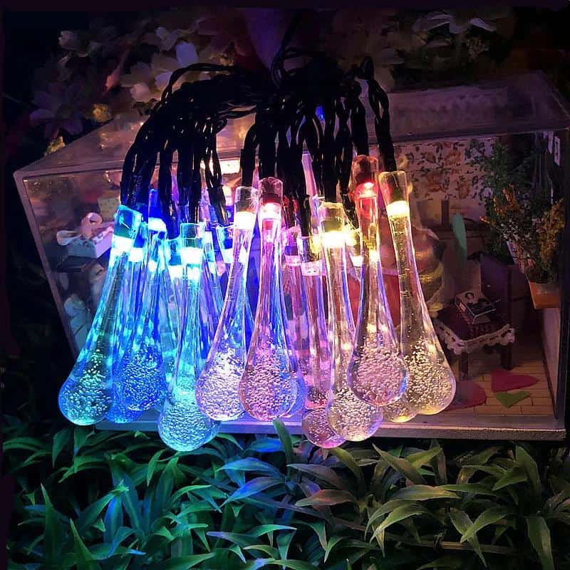 Colorful LED glass decanters illuminated with vibrant blue, pink, yellow, and white lights, displayed on a shelf surrounded by greenery and decorative items at Monalisa Store.