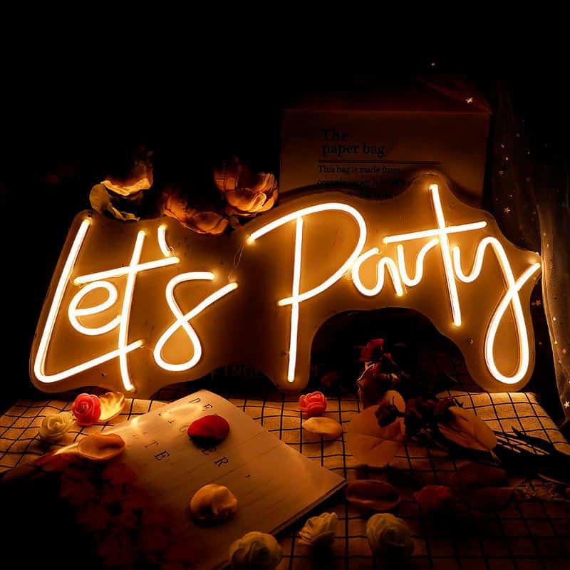 Fun party neon sign illuminated at night with scattered rose petals and a notebook on a checkered tablecloth for celebration decor.