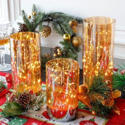 Golden candle holders with LED string lights for festive holiday decor at Monalisa Store. Elegant Christmas centerpiece with pinecones, ornaments, and greenery. Perfect for creating a warm, cozy atmosphere.
