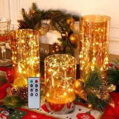 Warm white fairy lights in gold cylindrical candle holders, festive Christmas table decor with greenery and ornaments, remote control included for light control, perfect for holiday ambiance and interior Christmas decoration.