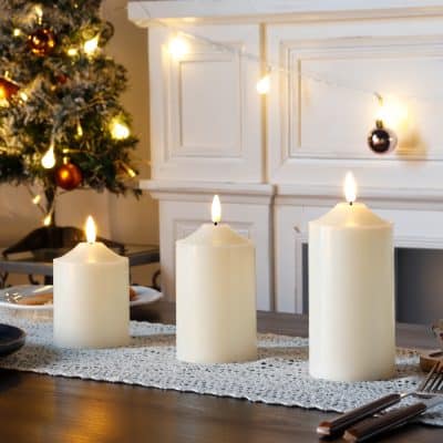 Soft white candles on a holiday dining table with Christmas tree in the background, creating a cozy and festive atmosphere. Perfect for holiday gatherings, home decor, and seasonal ambiance.