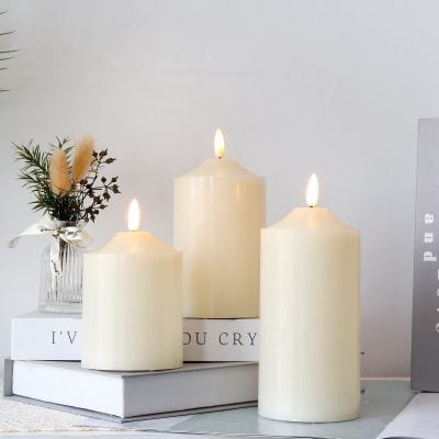 White scented candles with flickering flames, ideal for home decor and relaxation, positioned on a stylish table with decorative books and a small vase of dried flowers for aesthetic appeal.