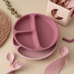 Silicone baby feeding plate with divided sections in pink, along with matching utensils and a storage container, perfect for toddler-friendly meals and easy cleaning.