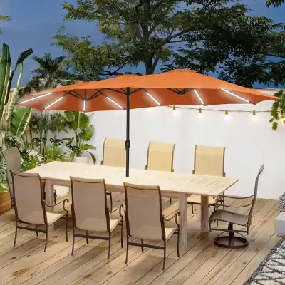 Stylish outdoor dining area with a large patio table, comfortable chairs, an orange umbrella, lush greenery, string lights, perfect for social gatherings or relaxing meals.