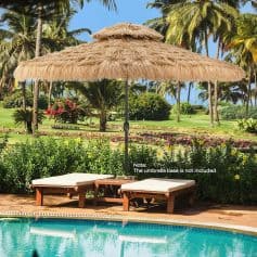Beachside poolside scene featuring a large straw umbrella with wooden lounge chairs beneath, surrounded by lush tropical greenery, vibrant flowers, and tall palm trees, creating a relaxing vacation atmosphere.