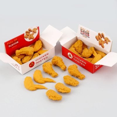 Crispy fried chicken nuggets and chicken drumsticks in red and white "Chicken Master" fast-food boxes with scattered pieces on white background.