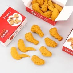 Crispy yellow chicken nuggets in red and white takeout boxes with scattered nuggets on a white surface.