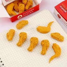 Chicken nuggets and chicken wing-shaped toy figures on a grid notebook with chicken snack boxes in the background.