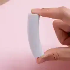 Silicone eyelash glue remover stick held between fingers on pink background, beauty skincare tool for eyelash extension removal, professional cosmetic accessory for lash care.